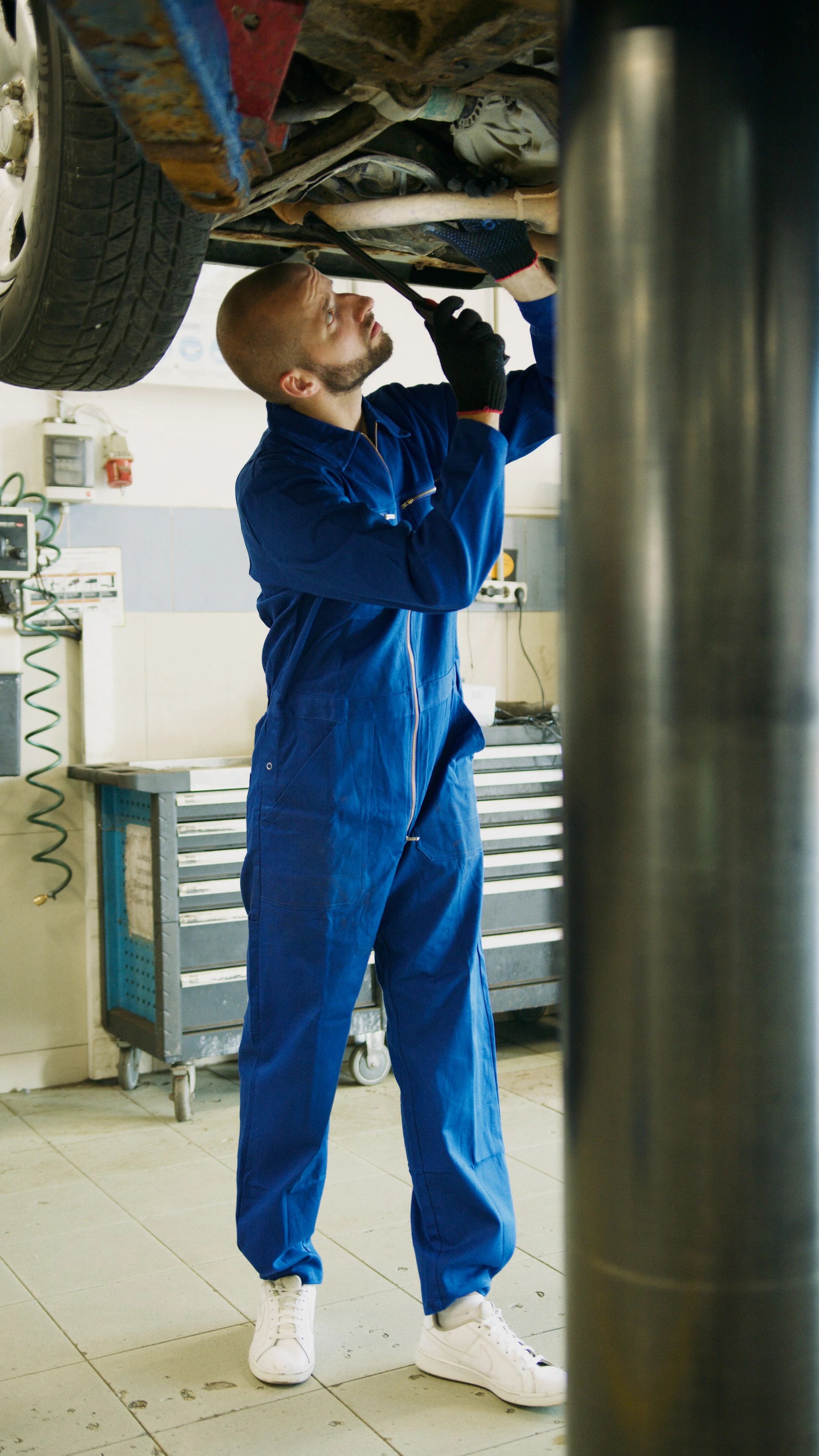 Auto mechanic in blue coveralls working underneath a car raised on a lift in a garage