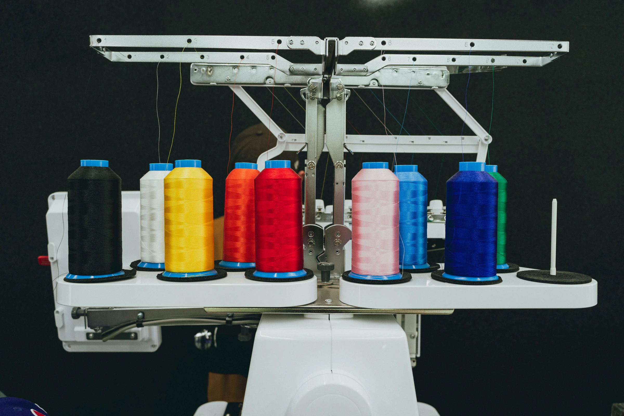 Commercial embroidery machine loaded with colorful thread cones in black, yellow, red, pink and blue
