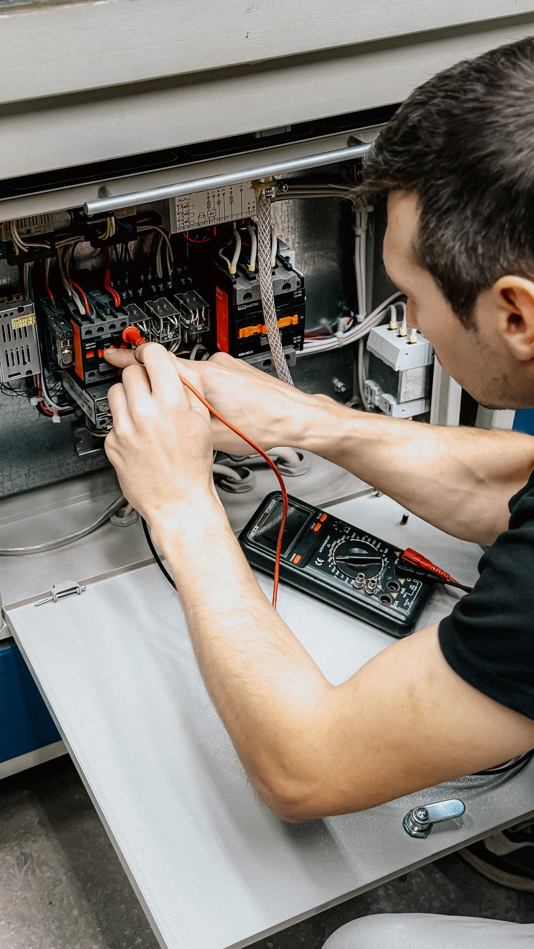 Electrician testing wiring in an open electrical control panel with a digital multimeter