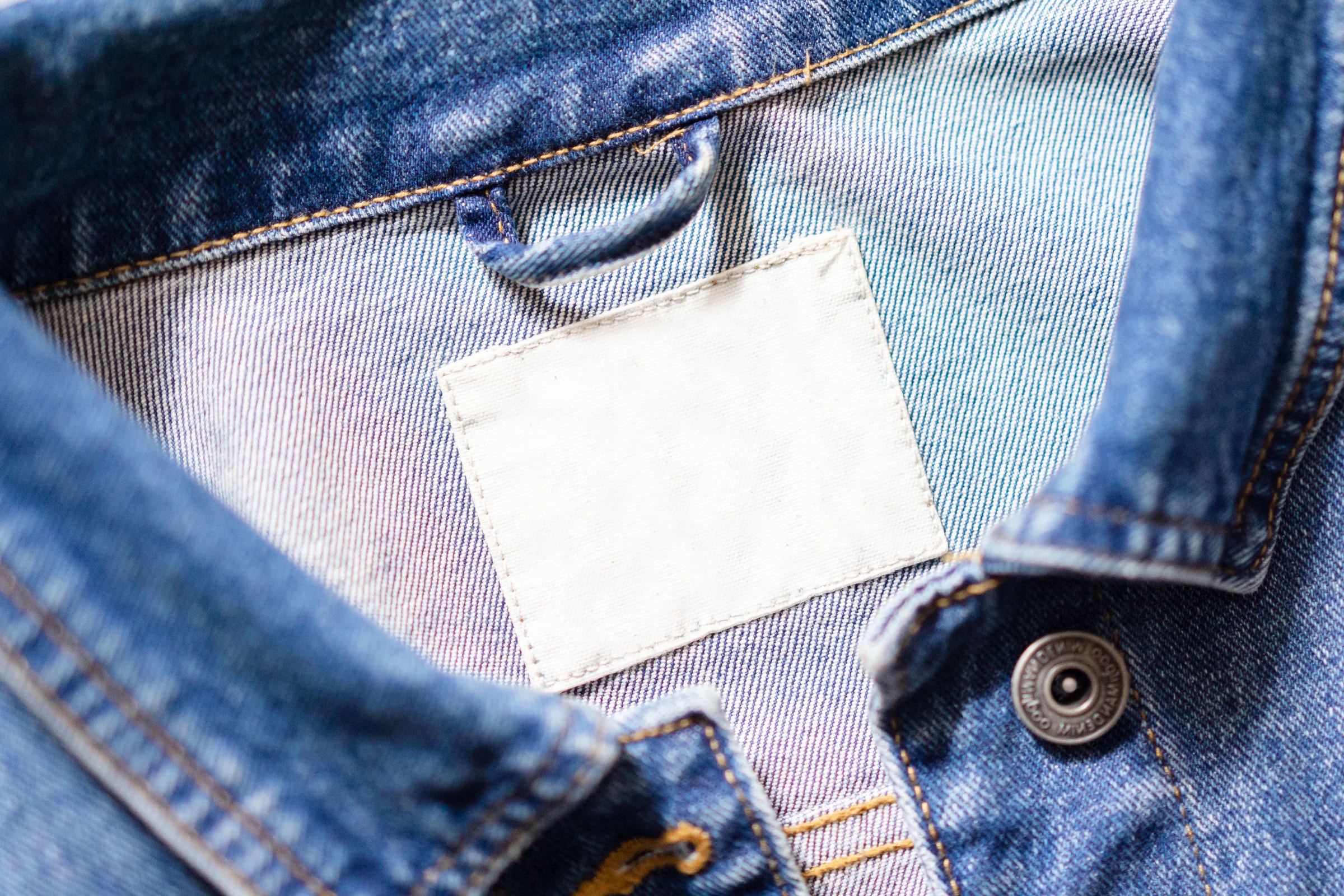 Close-up of a denim jacket collar with a blank white sewn-in label ready for custom branding