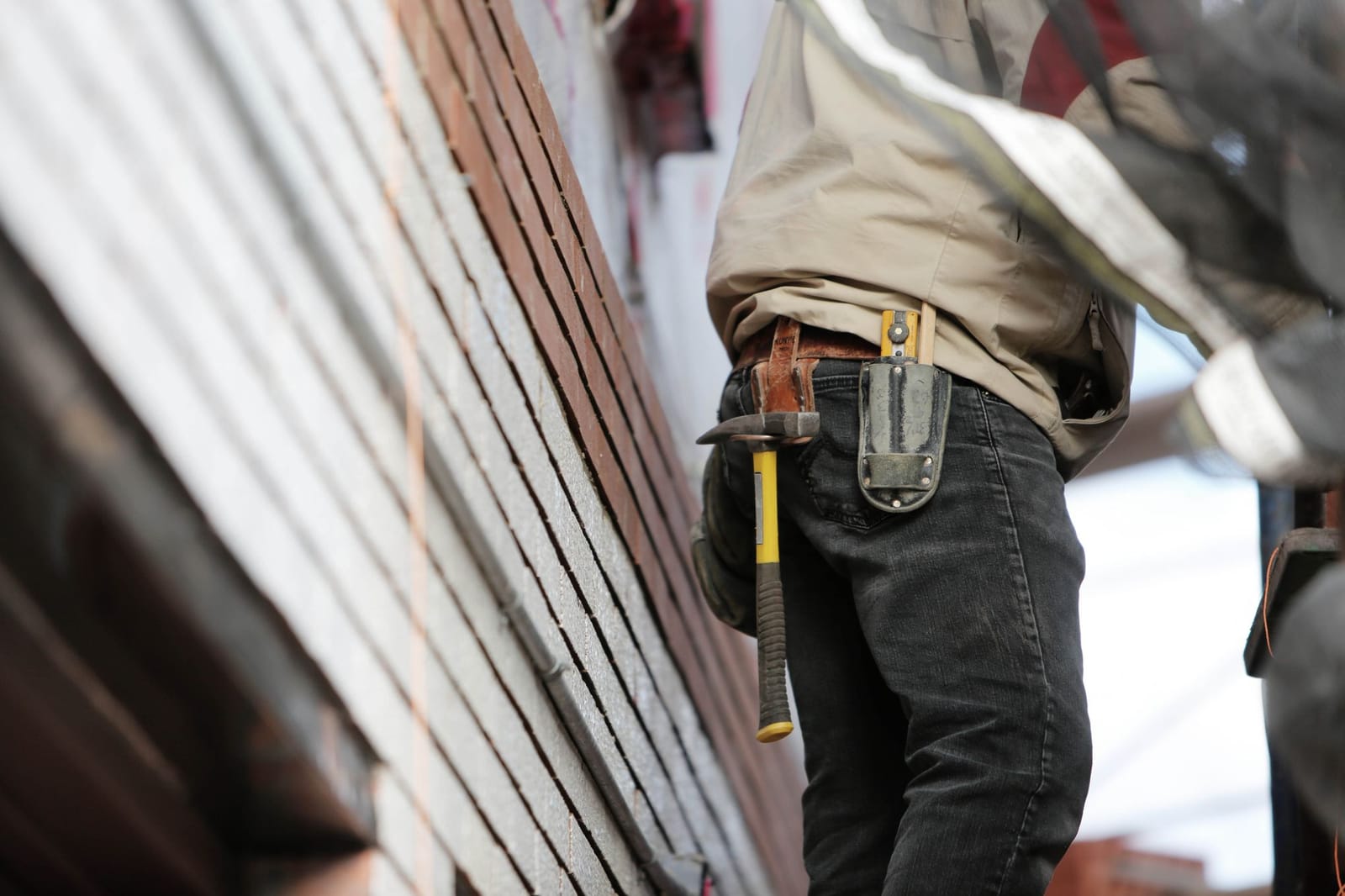 Construction worker in dark work pants with a hammer and tool holster on his belt at a job site