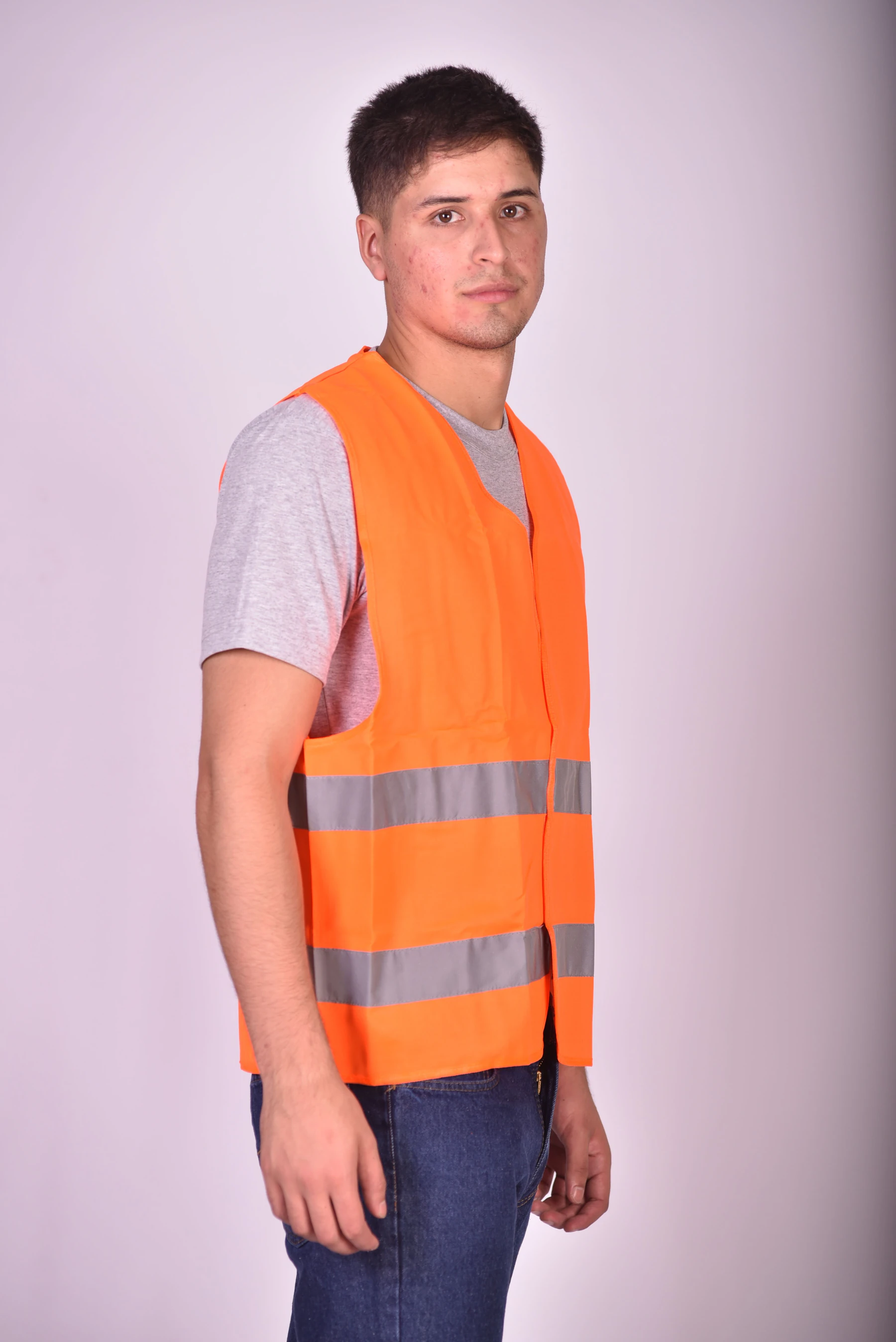 Young man wearing an orange safety vest with reflective silver stripes over a gray t-shirt