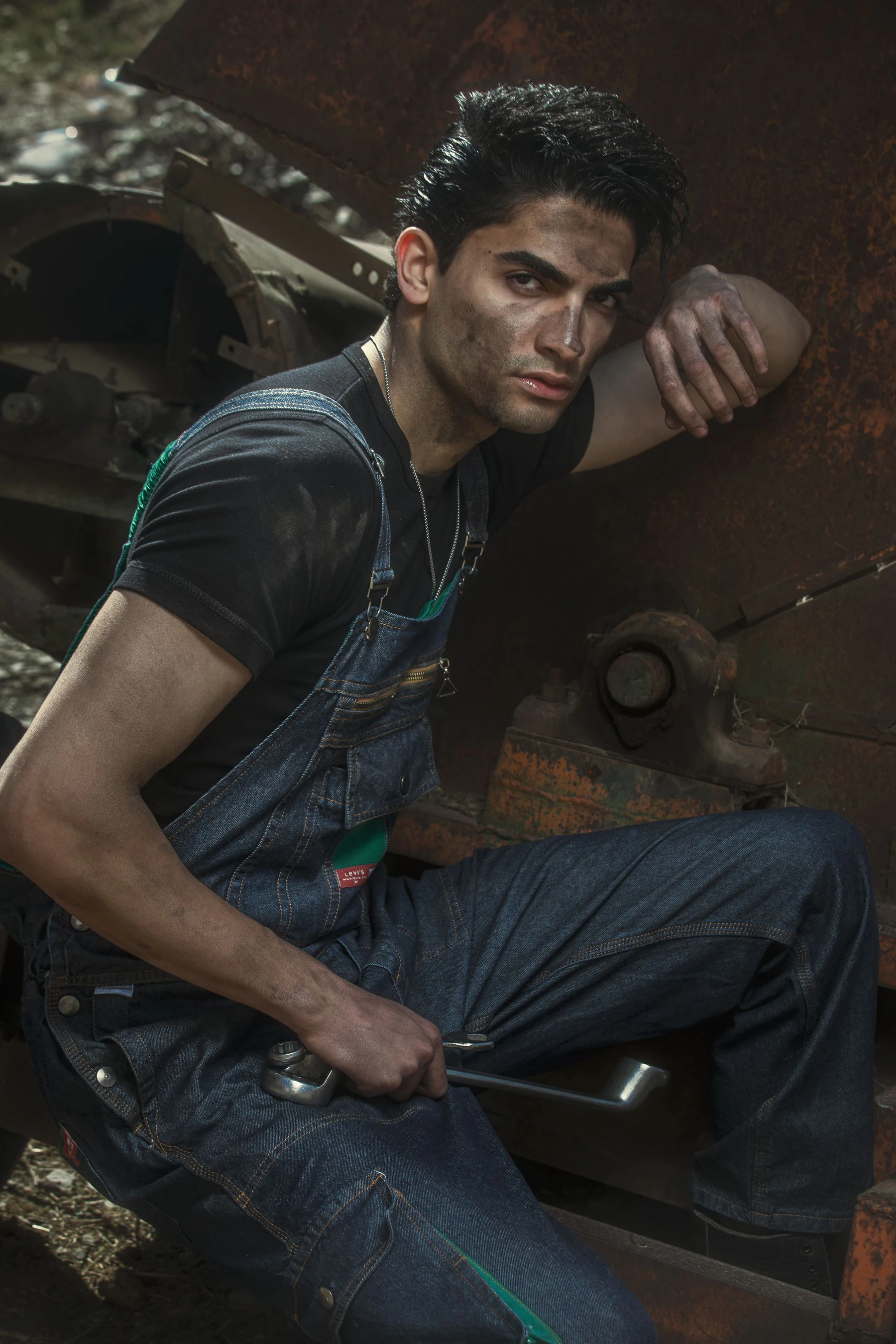 Mechanic wearing heavy blue denim bib overalls holding a wrench in a gritty industrial setting