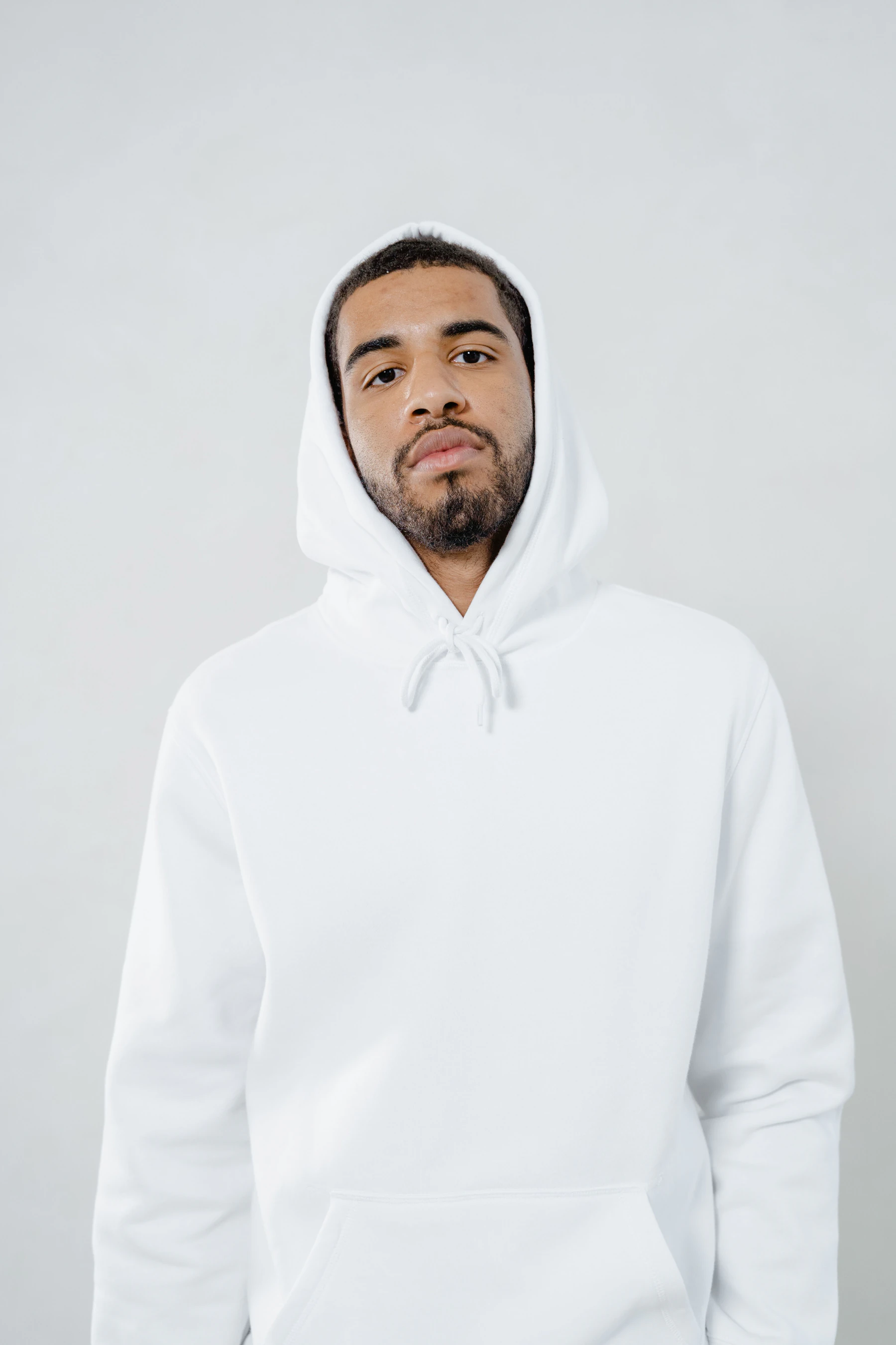 Bearded man wearing a plain white pullover hoodie with the hood up against a light gray background